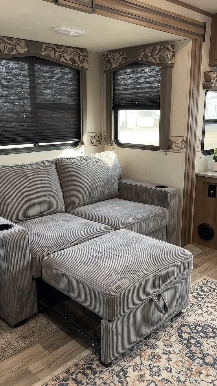 Grey striped sectional sofa and ottoman inside a camper with wood flooring.