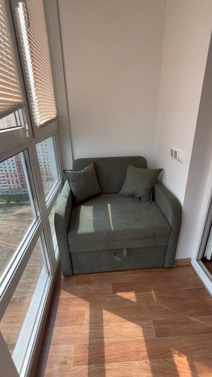 Olive green armchair with cushions in a small room corner by a window