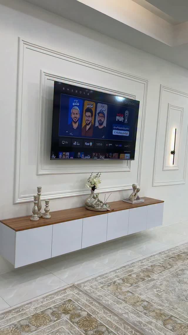 Wall-mounted television above a white and wood console table with a patterned rug.