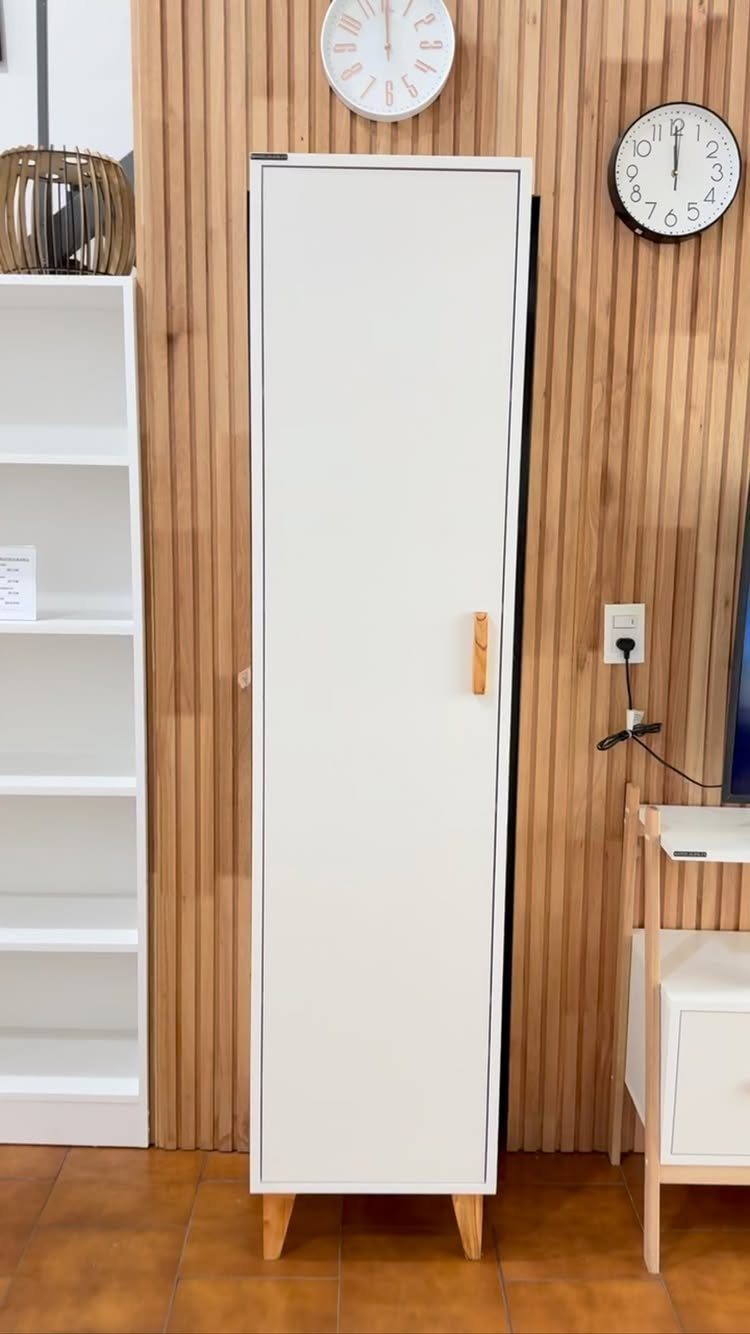 Tall white narrow cabinet with wooden legs against a wooden slat wall