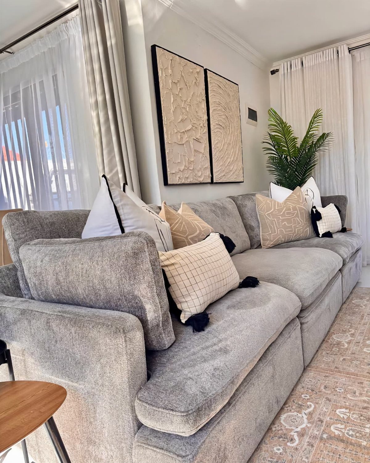Gray sectional sofa with beige pillows and textured wall art in a bright room.