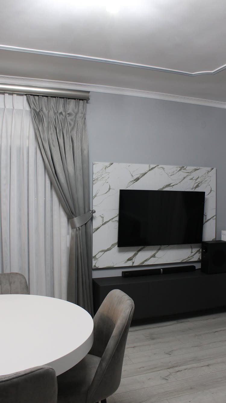 Gray living room with marble wall panel, flat-screen TV, and gray upholstered chairs.