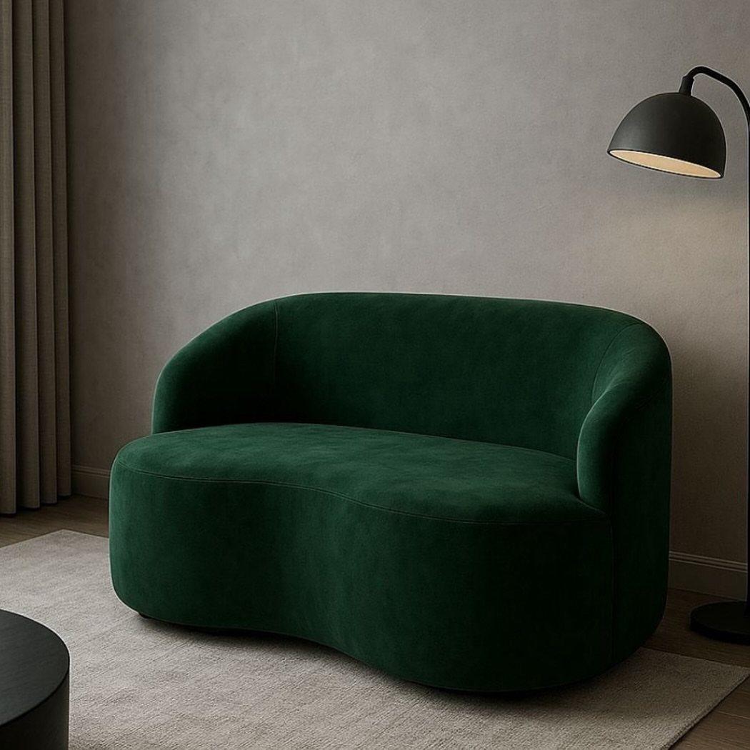 Dark green velvet curved couch in a minimalist living room with a black lamp.