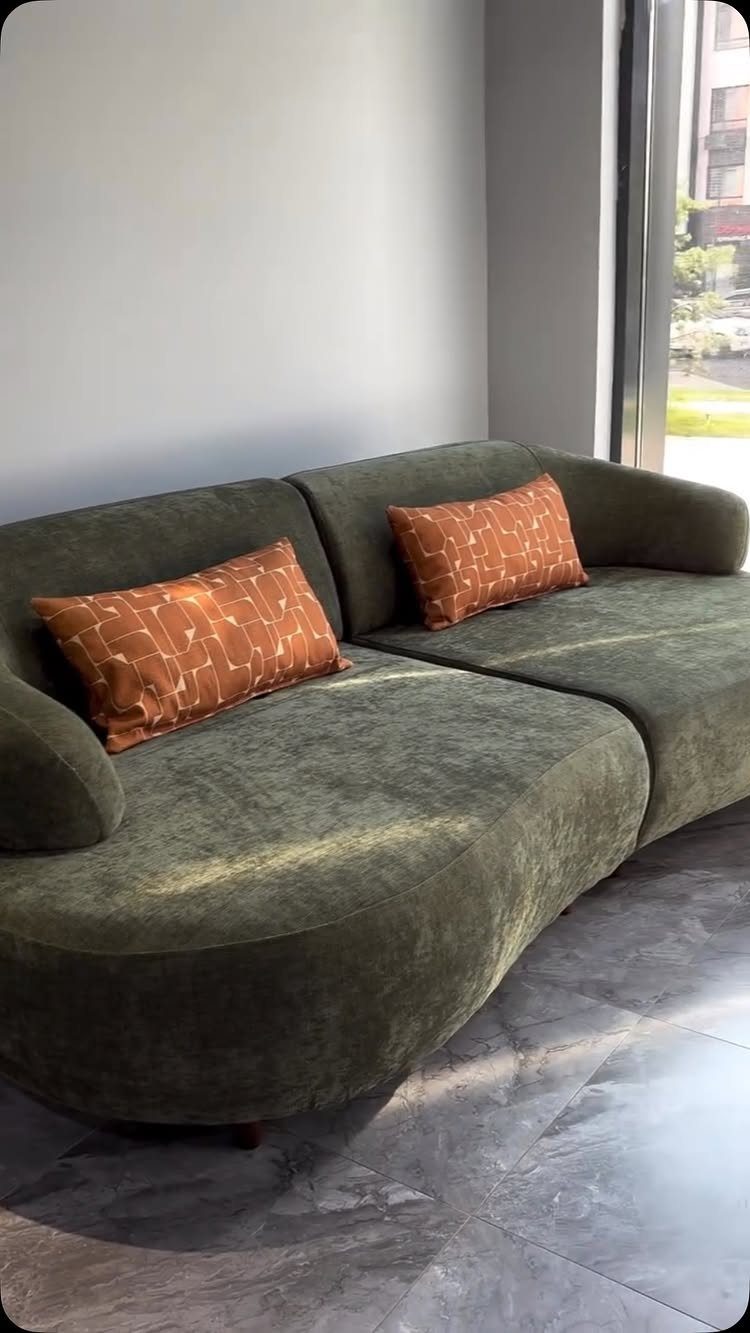 Olive green velvet curved sofa with two orange patterned accent pillows.