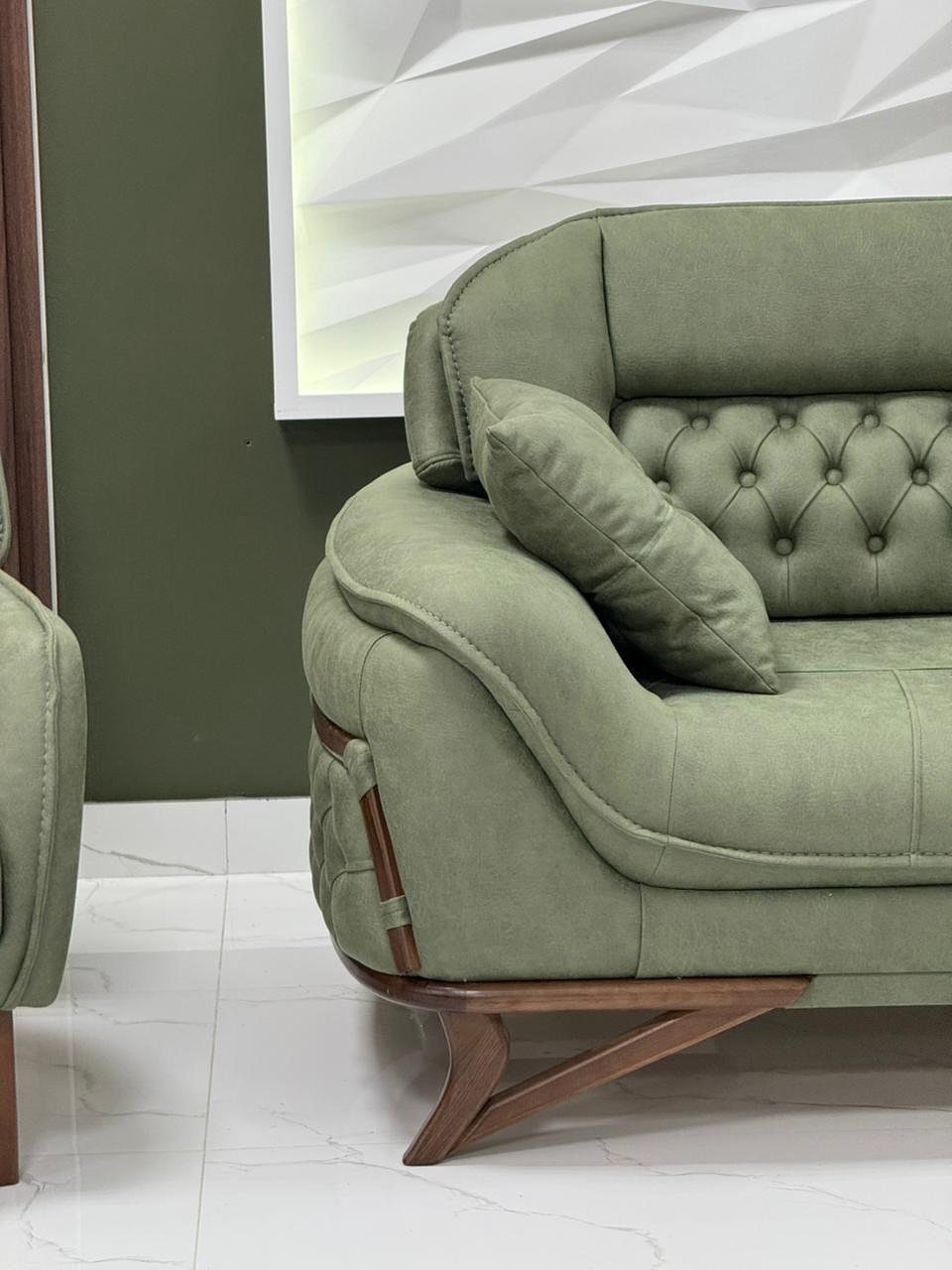Sage green tufted couch with wooden legs against a dark green wall.