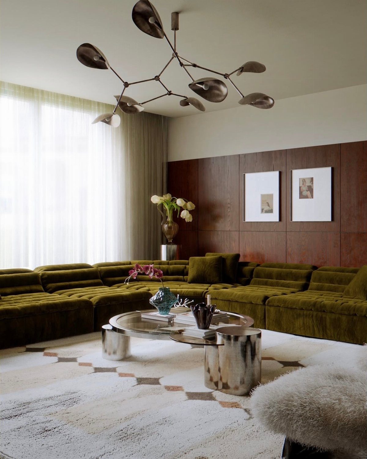 Olive green velvet sectional sofa with a sculptural silver coffee table and branch-like lighting.