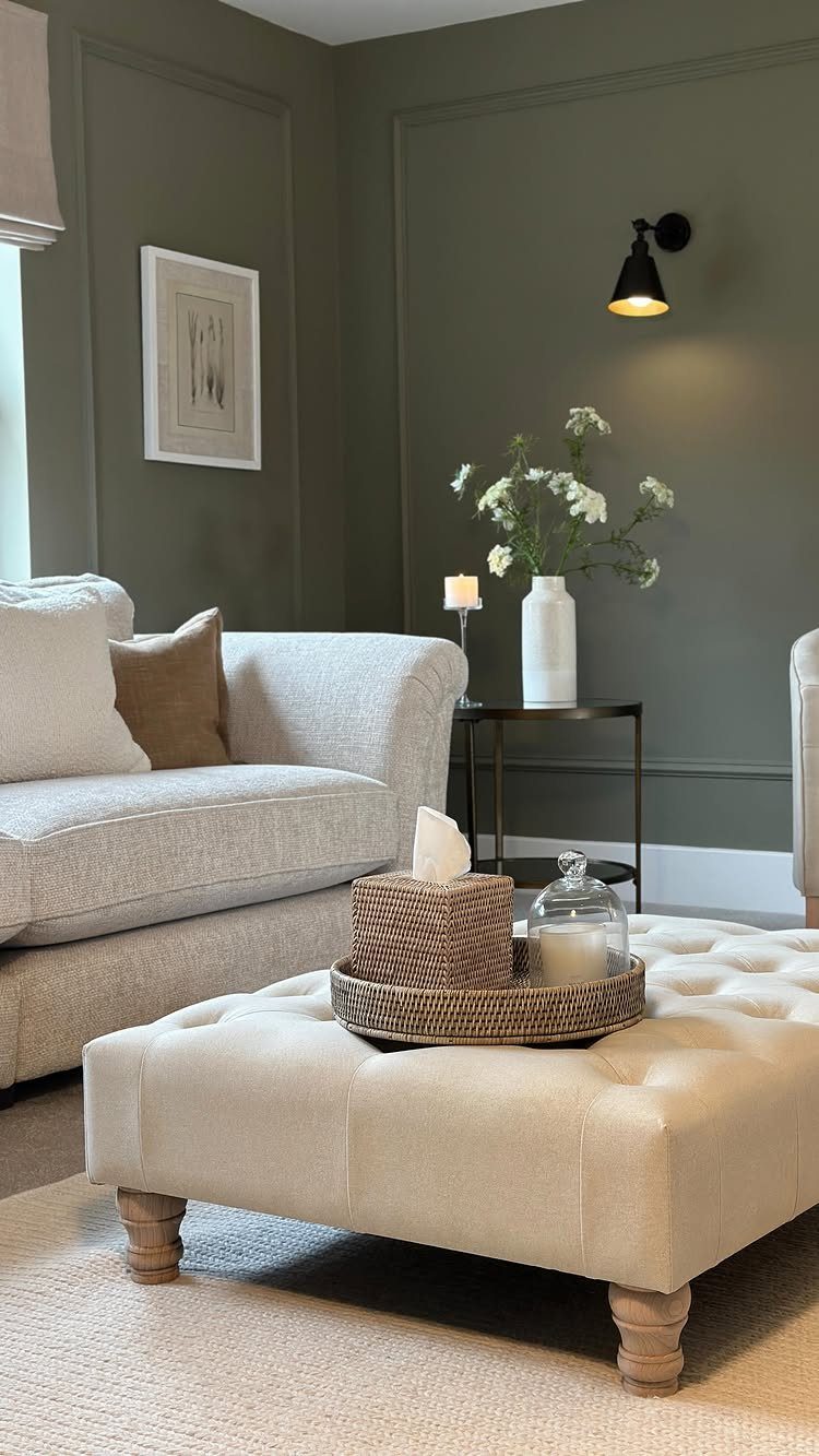 Olive green walls with molding in a living room with beige furniture and flowers.