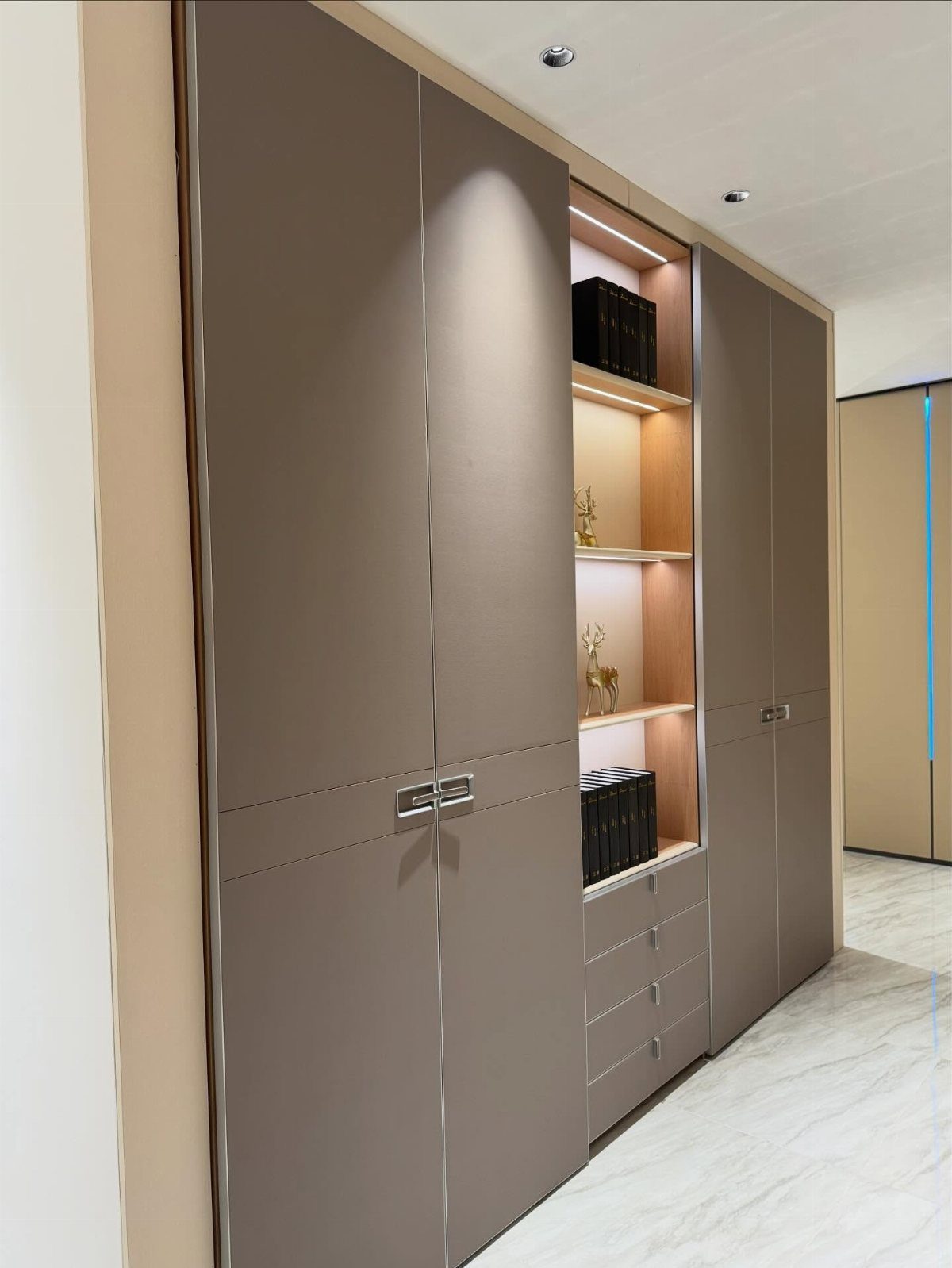 Modern taupe built-in wardrobe with integrated lighting and open shelving on marble floor