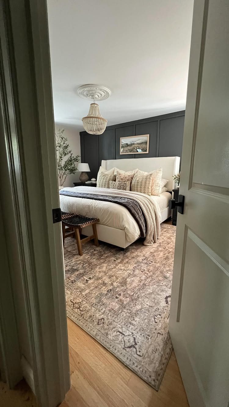White upholstered bed with layered decorative pillows and a neutral patterned area rug.