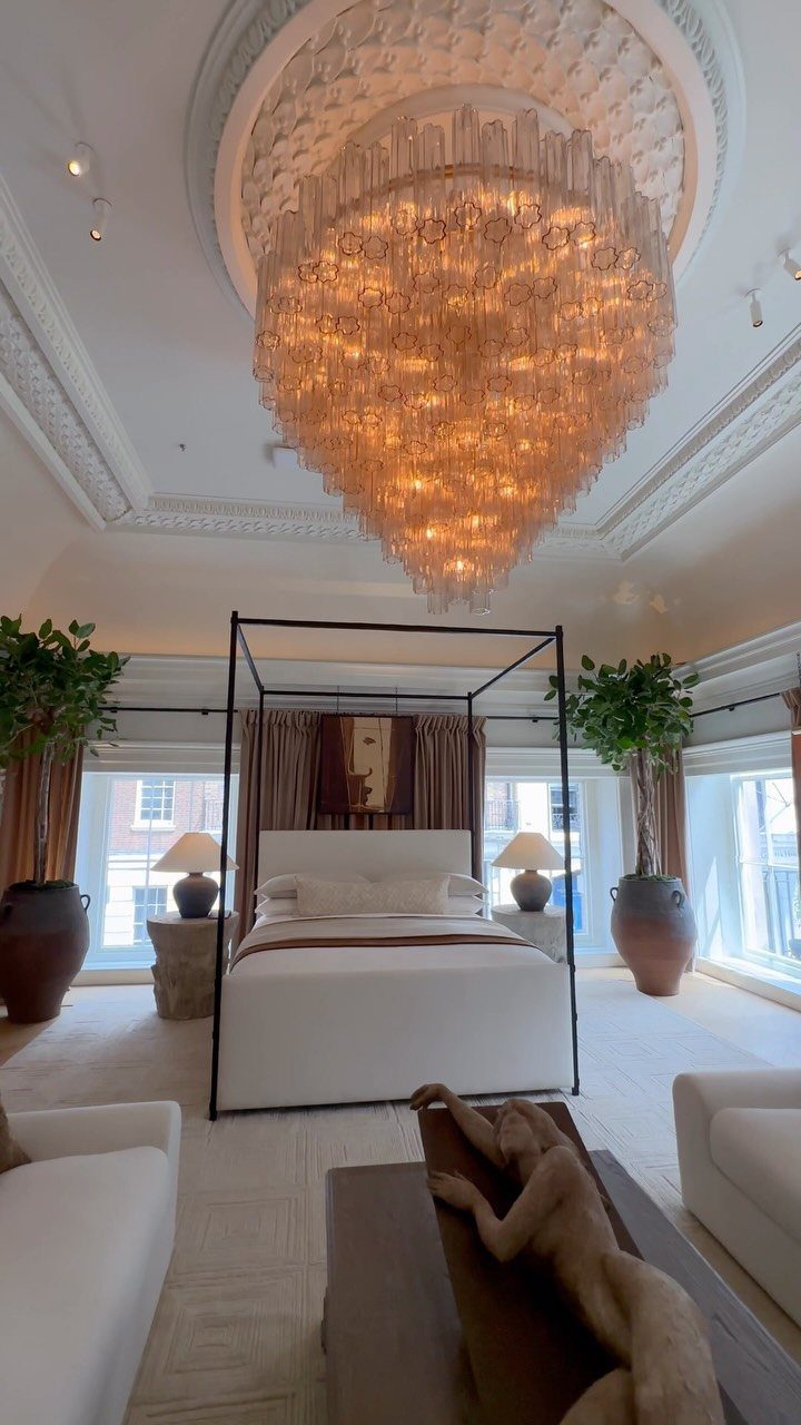 Black four-poster bed with white linens under a large crystal chandelier in luxury bedroom
