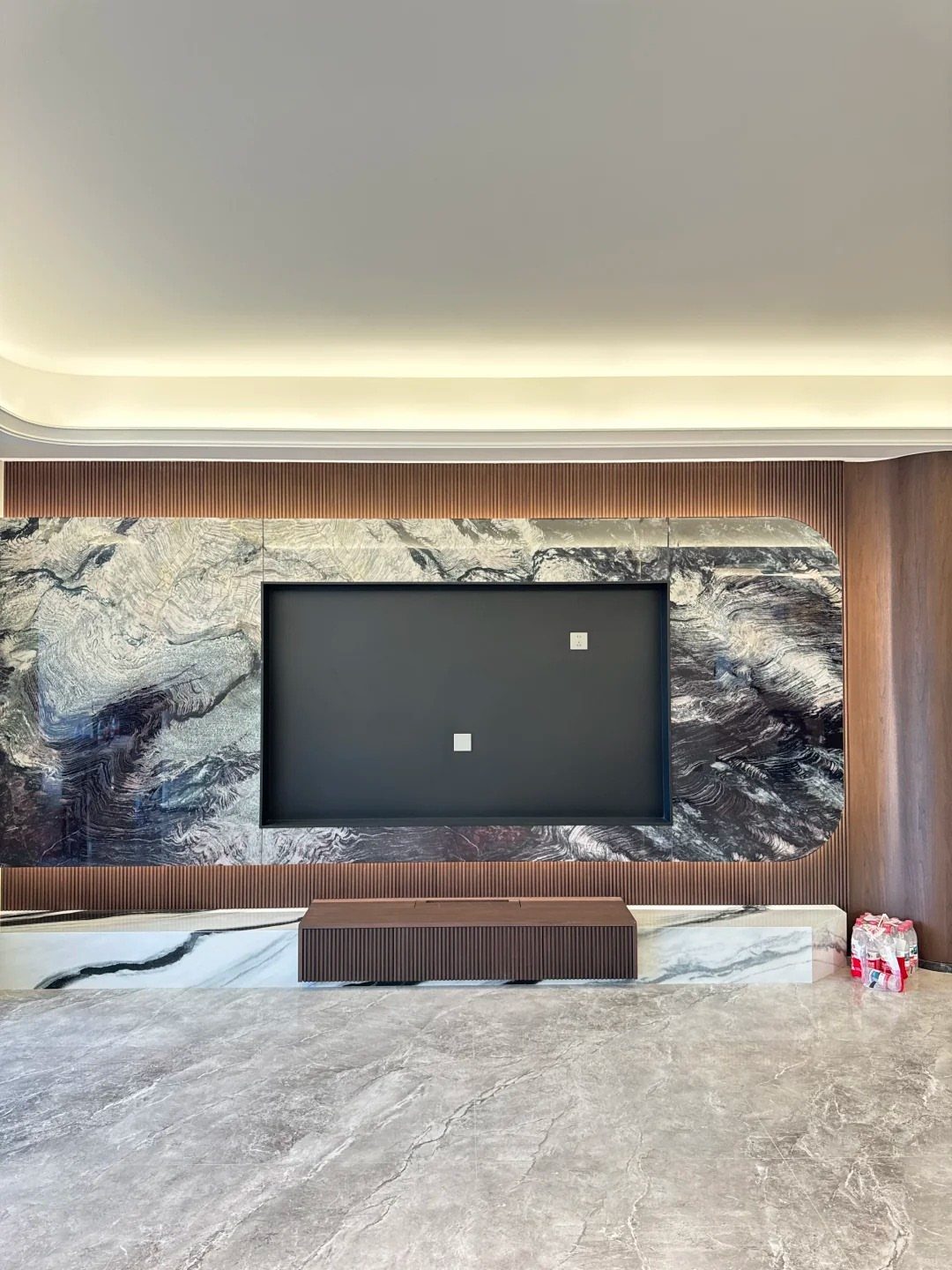 Modern living room with a large TV, marble walls, and wooden furniture.