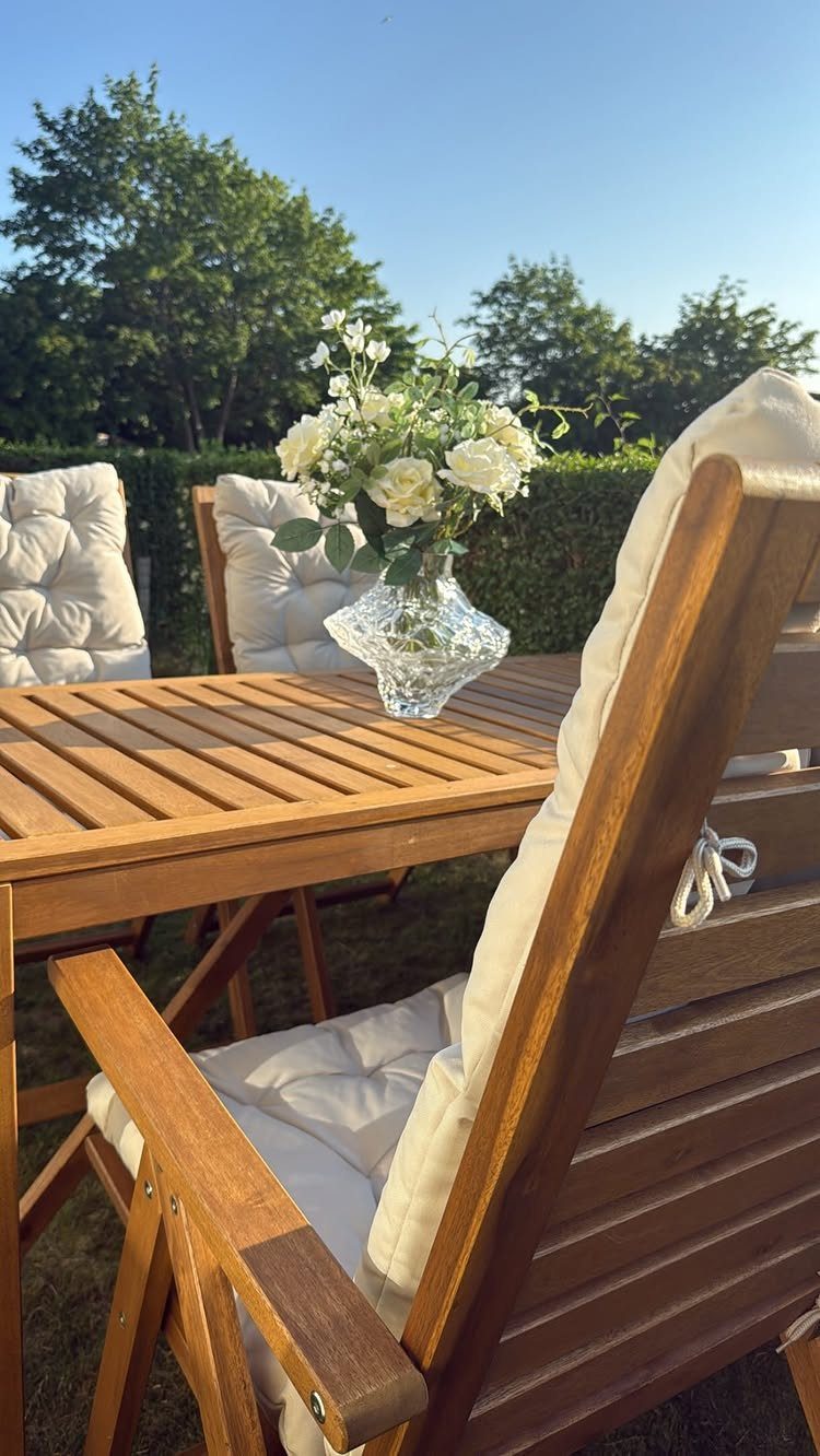 Wooden outdoor dining set with white tufted cushions and white flowers in vase