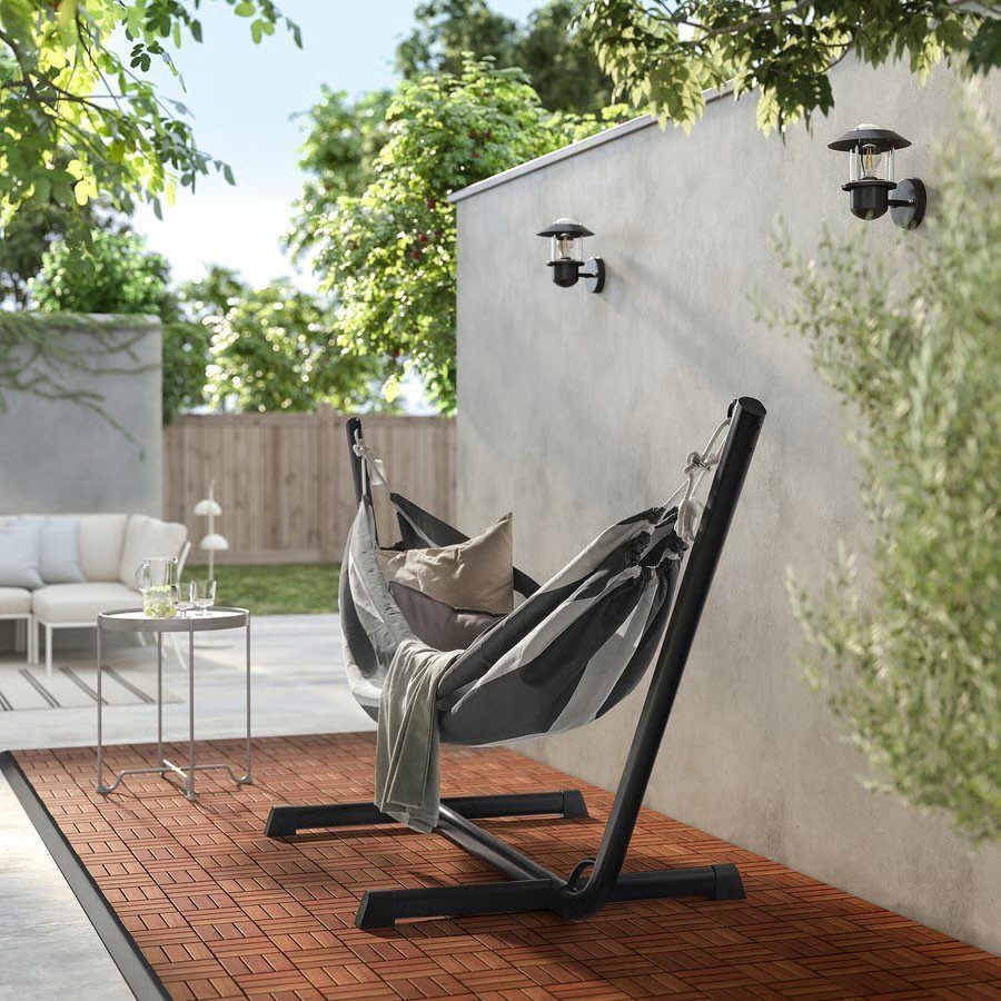 Striped hammock on a black stand set on wooden decking tiles outdoors.