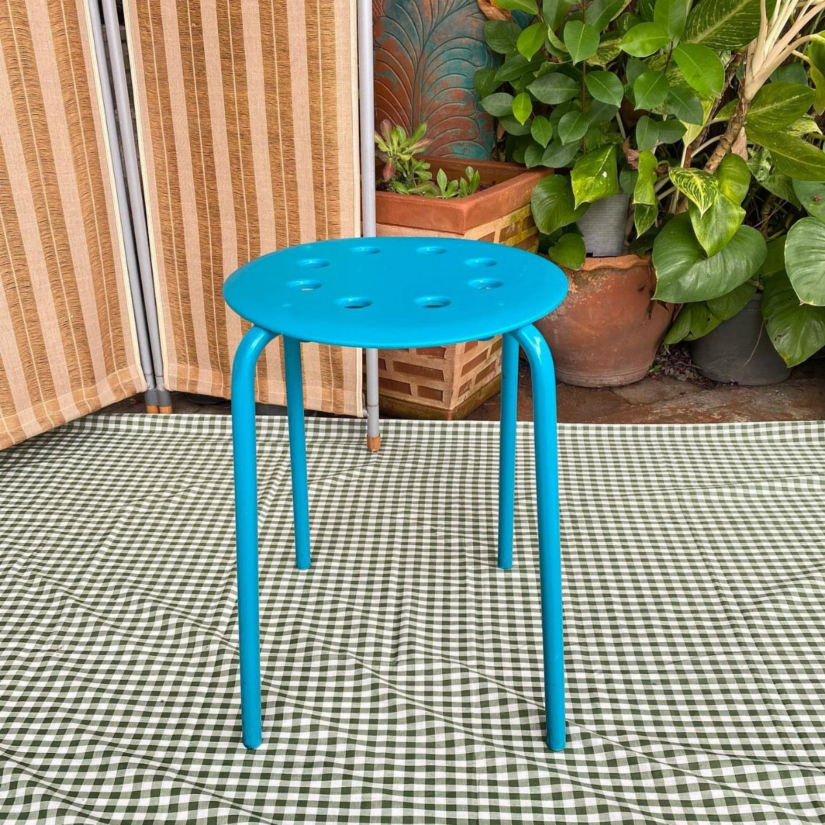 Blue metal stool with perforated seat on a green checkered outdoor rug