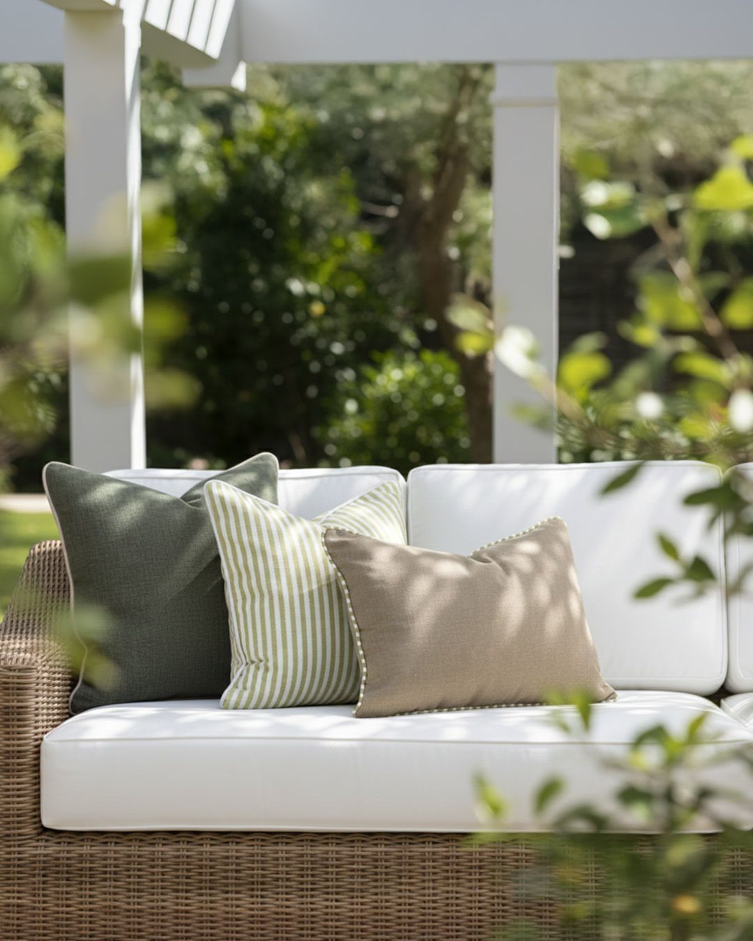 Wicker outdoor sofa with white cushions and green and beige decorative pillows.