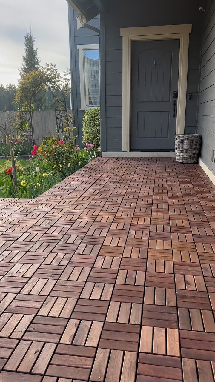 Brown wooden interlocking deck tiles covering a porch area outside a grey house.