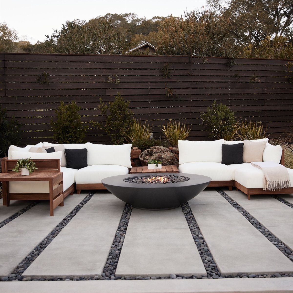 White modular outdoor sofas and a black fire pit on a concrete patio