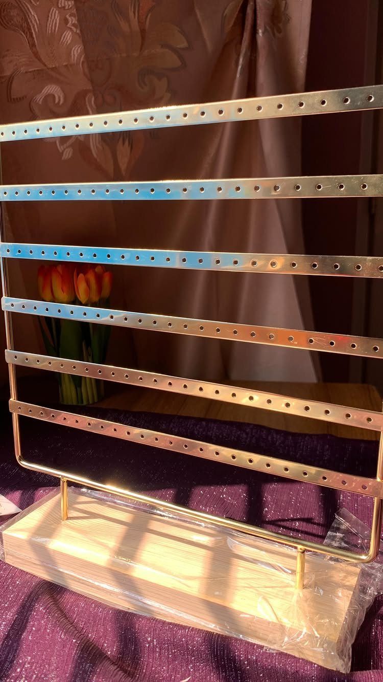 Gold metal earring stand with perforated bars on a wooden base.