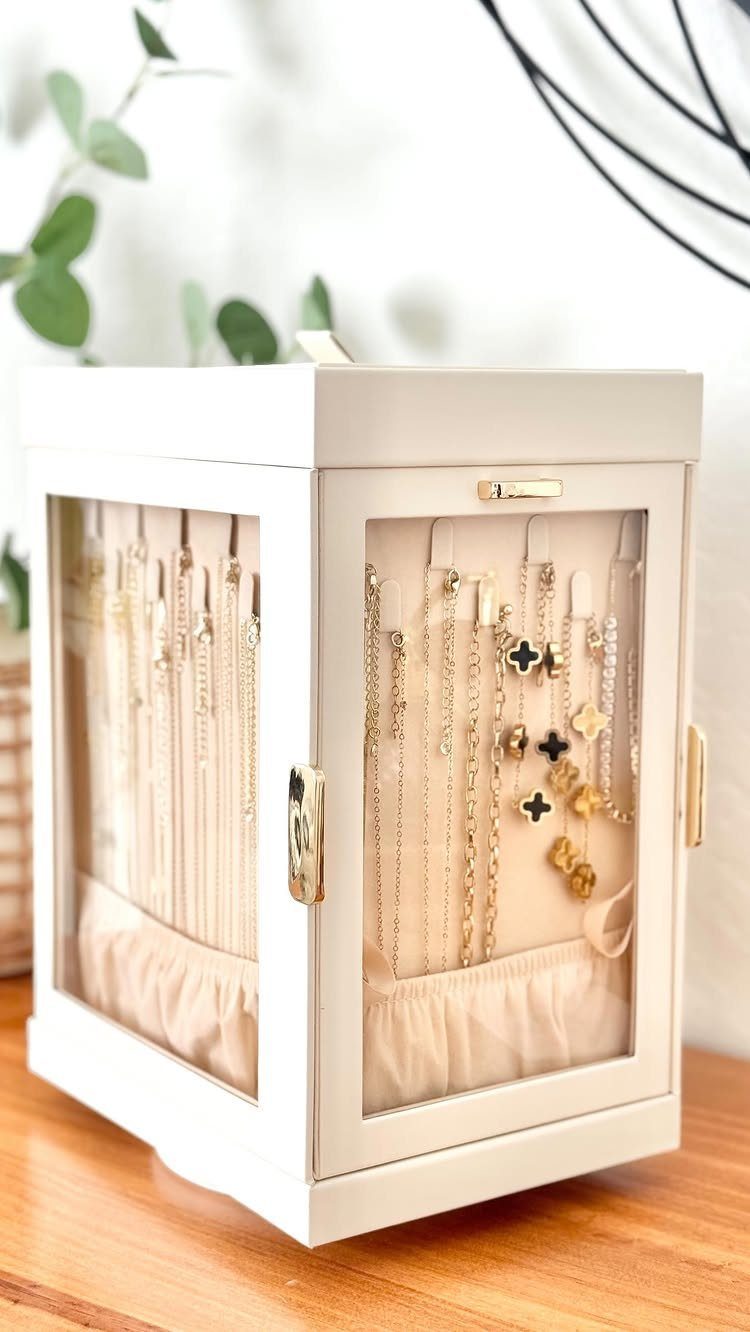 White glass-paneled jewelry box displaying gold necklaces and earrings on a wooden table