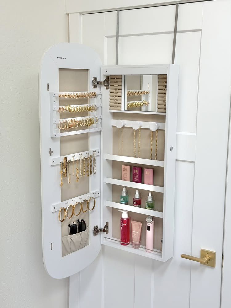 White wall-mounted jewelry armoire open to reveal organized gold jewelry and beauty products.