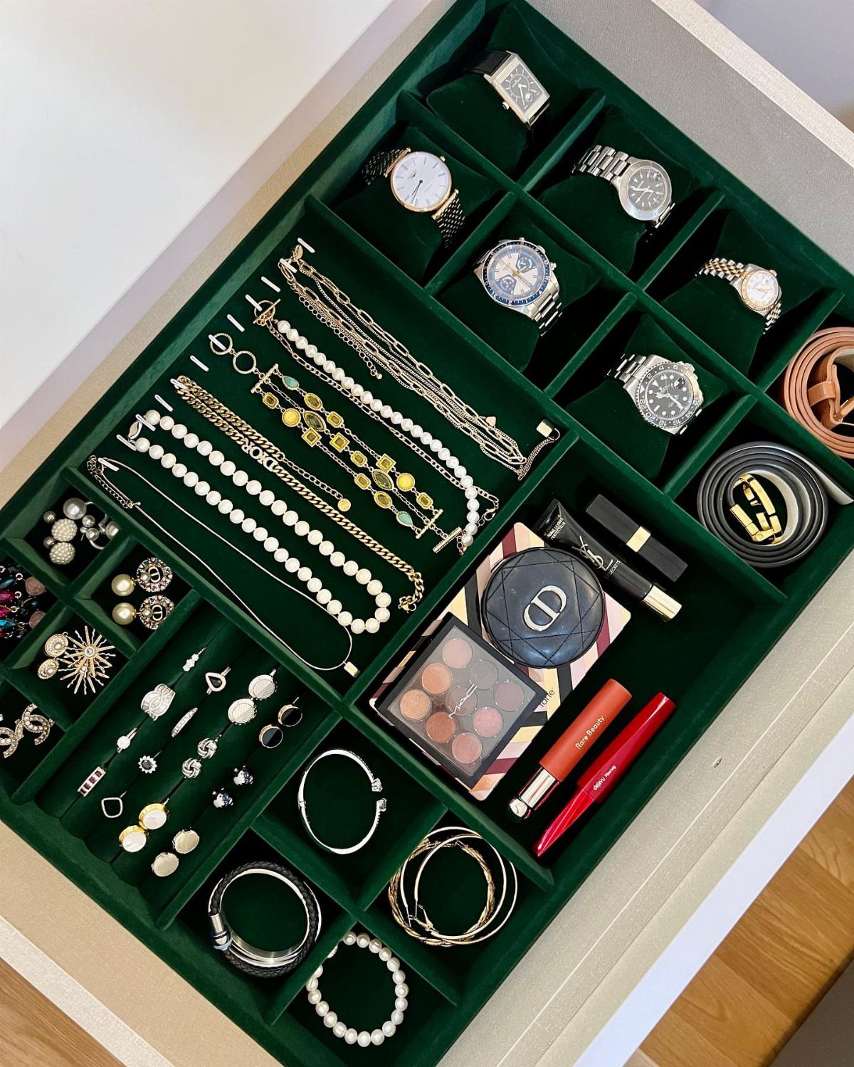 Green velvet jewelry tray in a drawer holding watches, necklaces, and makeup.