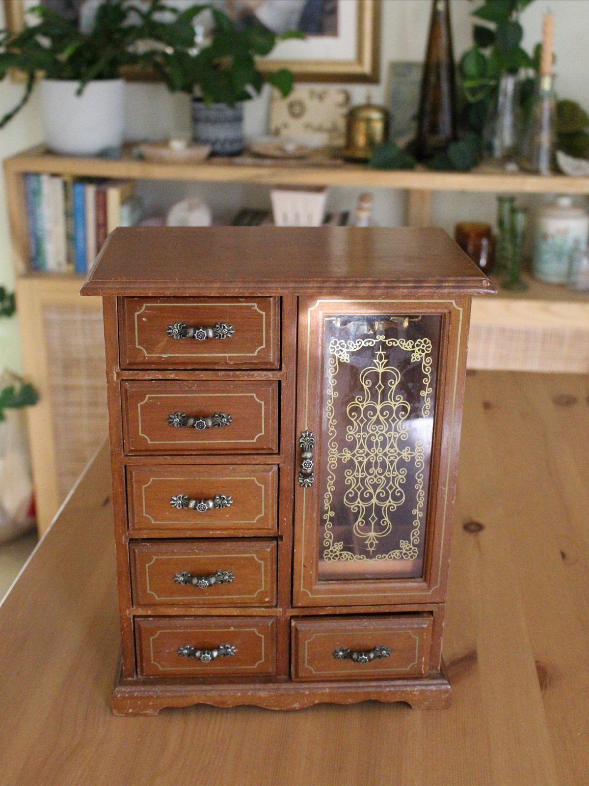 Vintage wooden jewelry chest with small drawers and a decorative glass cabinet door.