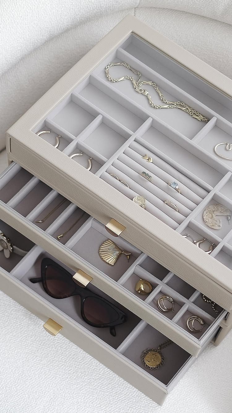 Stackable grey jewelry boxes with multiple drawers holding rings, necklaces, and sunglasses.