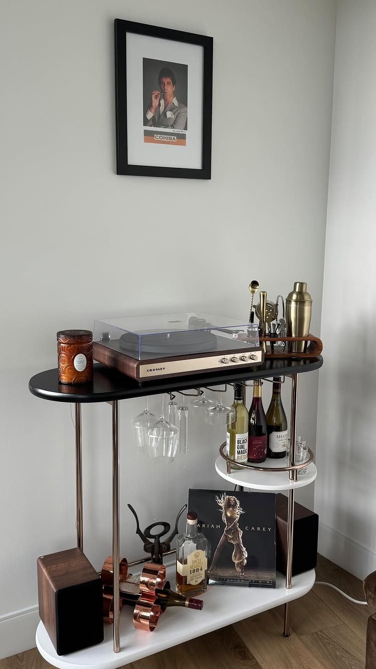 Gold-framed bar cart with a record player, wine bottles, and liquor in a corner.