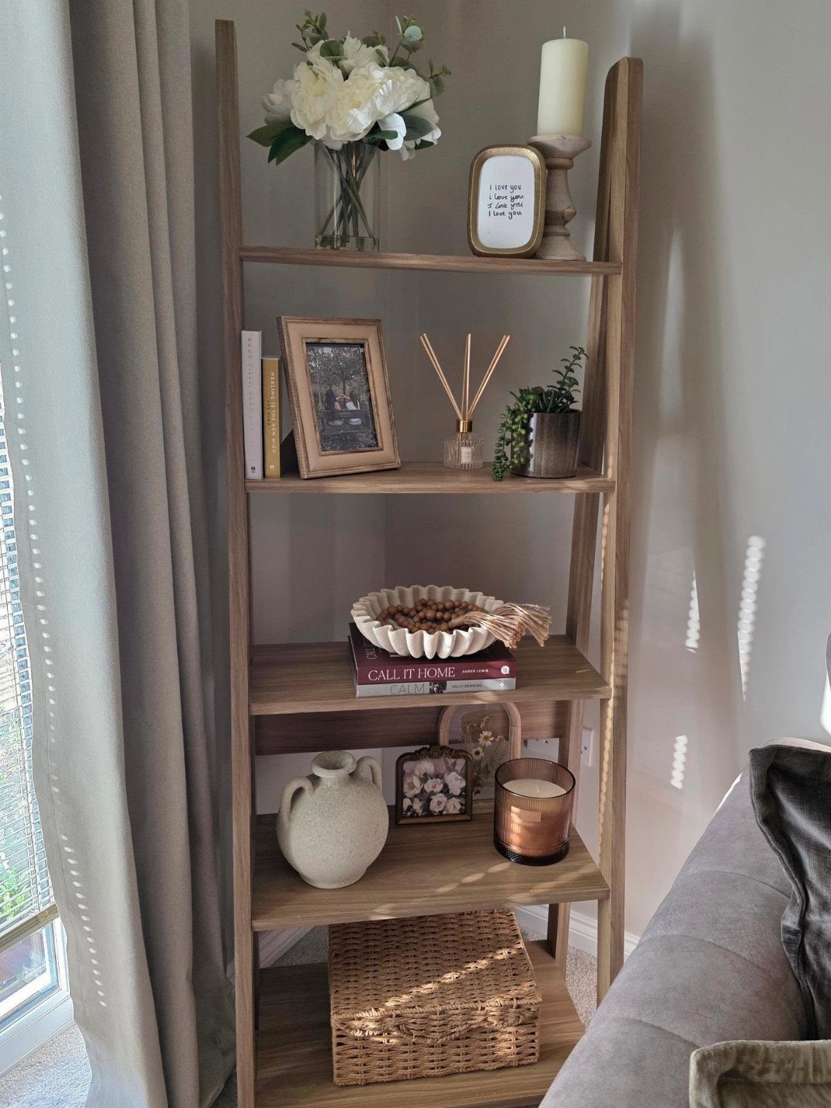 Wooden leaning ladder shelf with decorative home accessories and plants against a white wall.