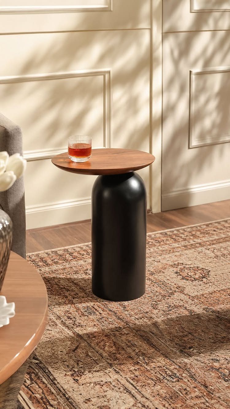 Small round side table with wooden top and black base on a patterned rug.