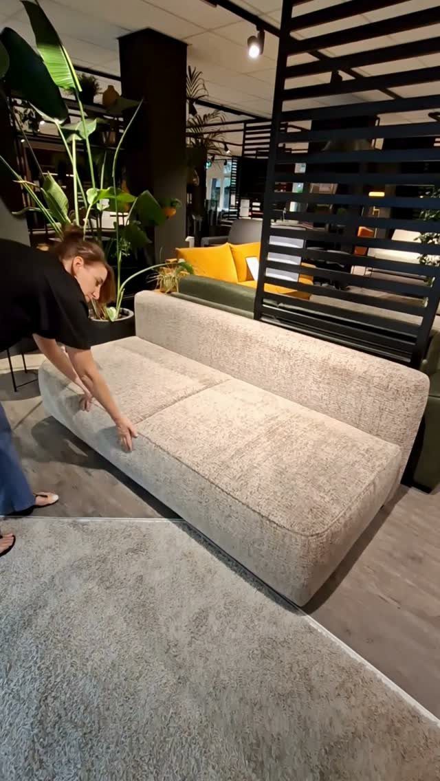 Woman touching a light beige armless fabric sofa in a modern furniture showroom