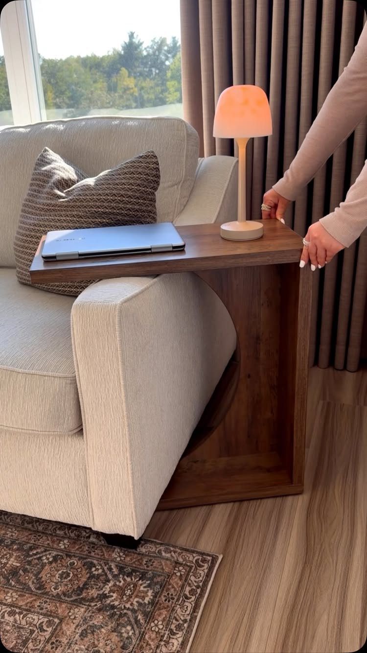 Beige fabric sofa with a wooden C-shaped side table holding a laptop and lamp.