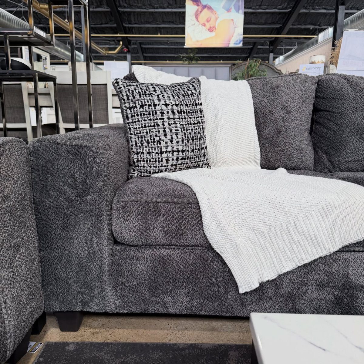 Dark grey fabric sofa with a white knit throw and patterned accent pillow.