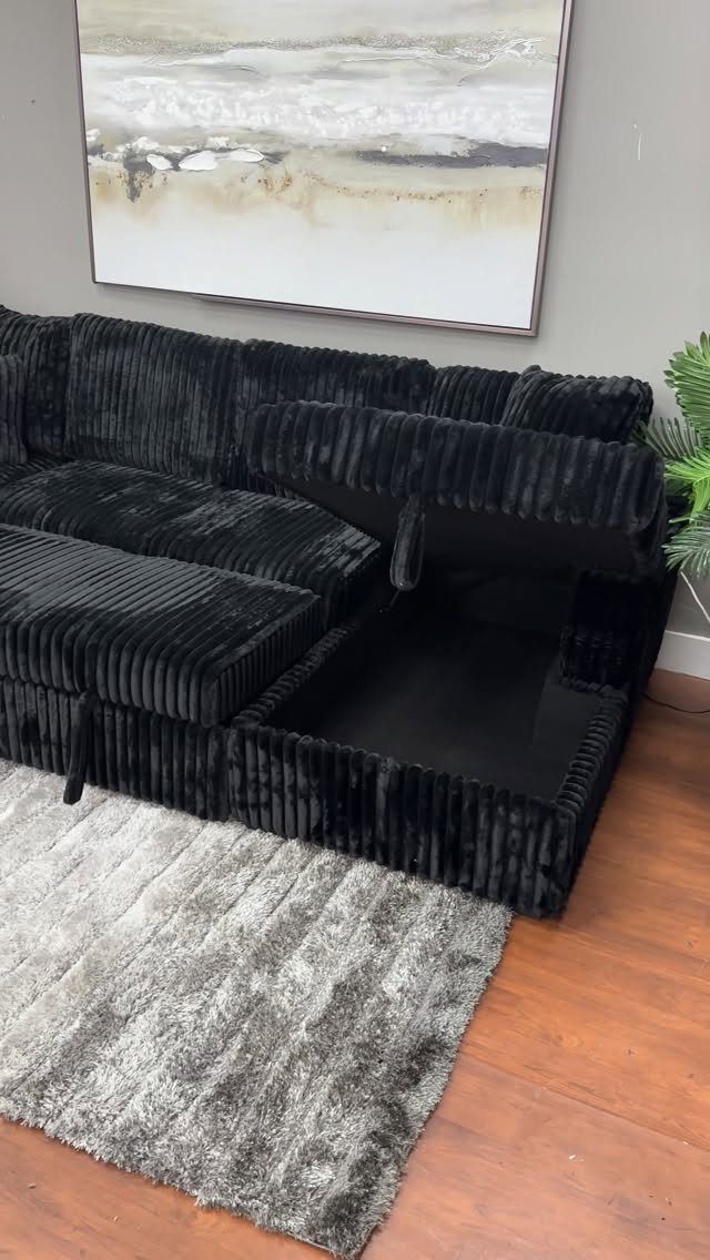 Black ribbed sectional sofa with an open storage compartment under the seat cushion.