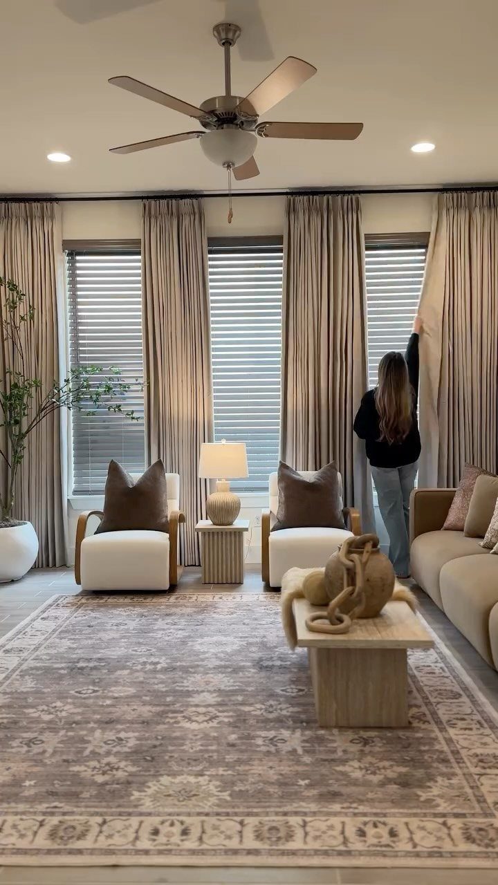 Beige floor-to-ceiling curtains in a living room with a woman adjusting them.