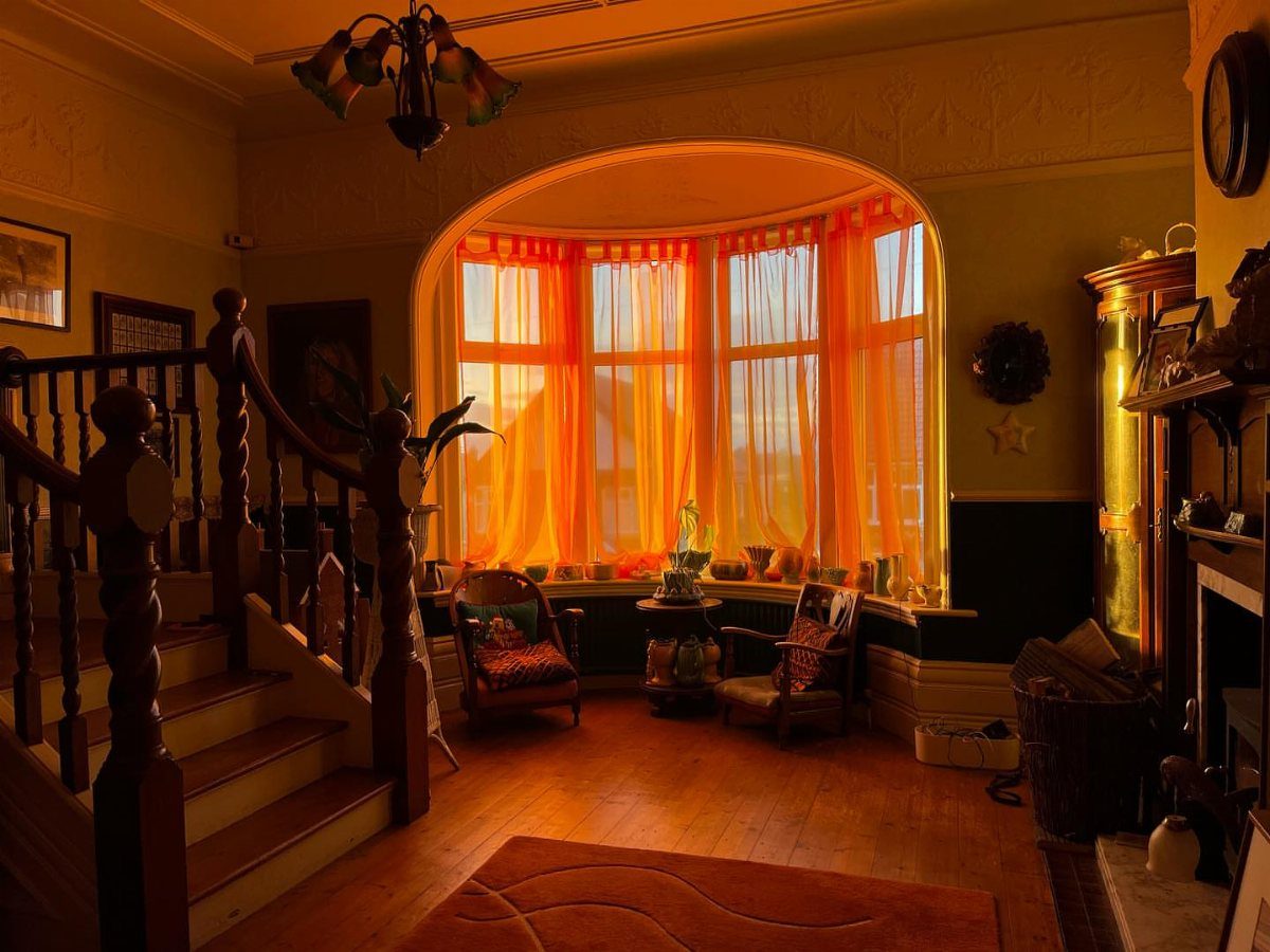 Tangerine orange curtains hanging in a bay window of a warm living room.