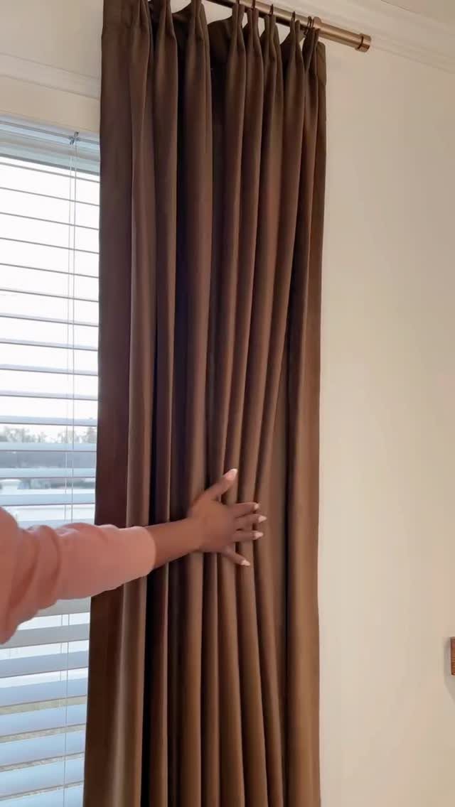 Brown velvet curtains hanging from a gold rod over white window blinds.