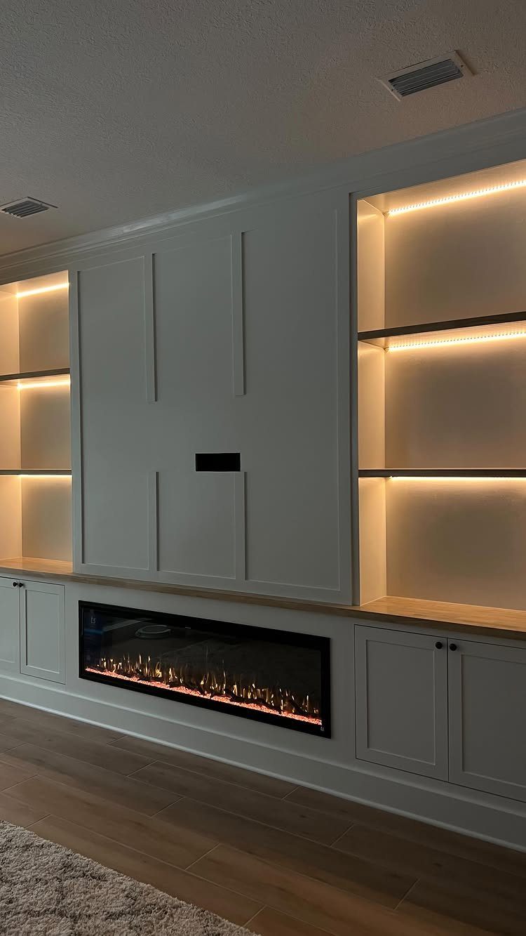 Modern white built-in wall unit with a linear fireplace and illuminated shelving cabinets.