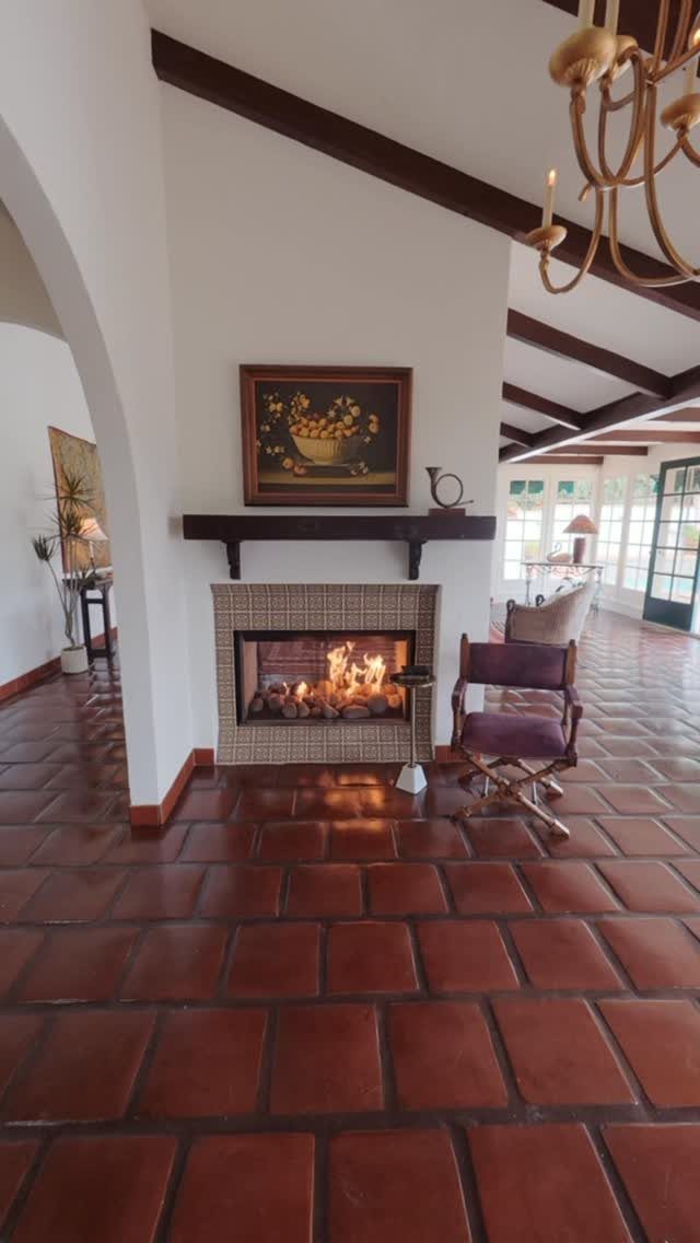 Fireplace with a small mosaic tile surround, dark wood mantel, and terracotta floors.