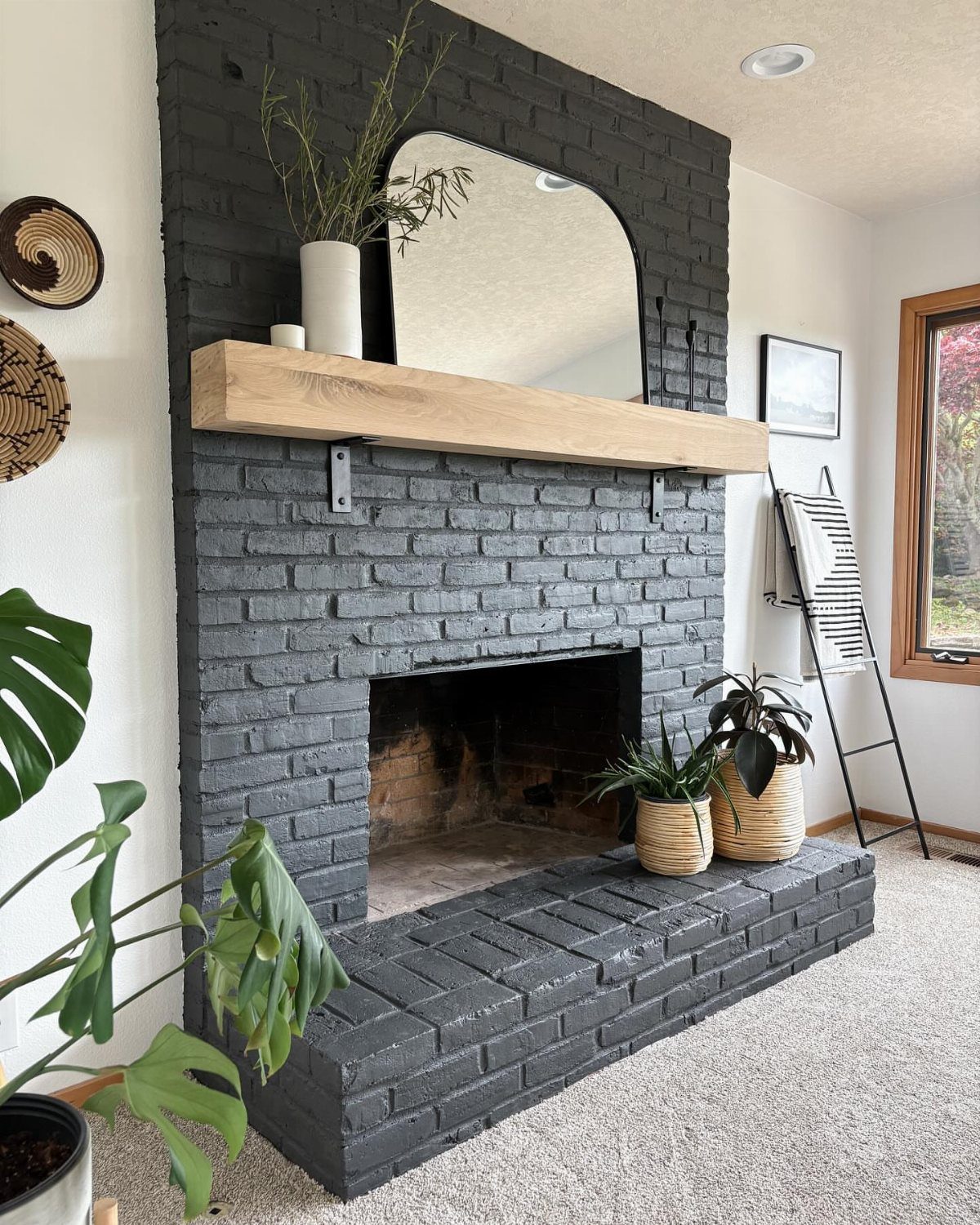 Dark grey painted brick fireplace with a light wood mantel and arched mirror.