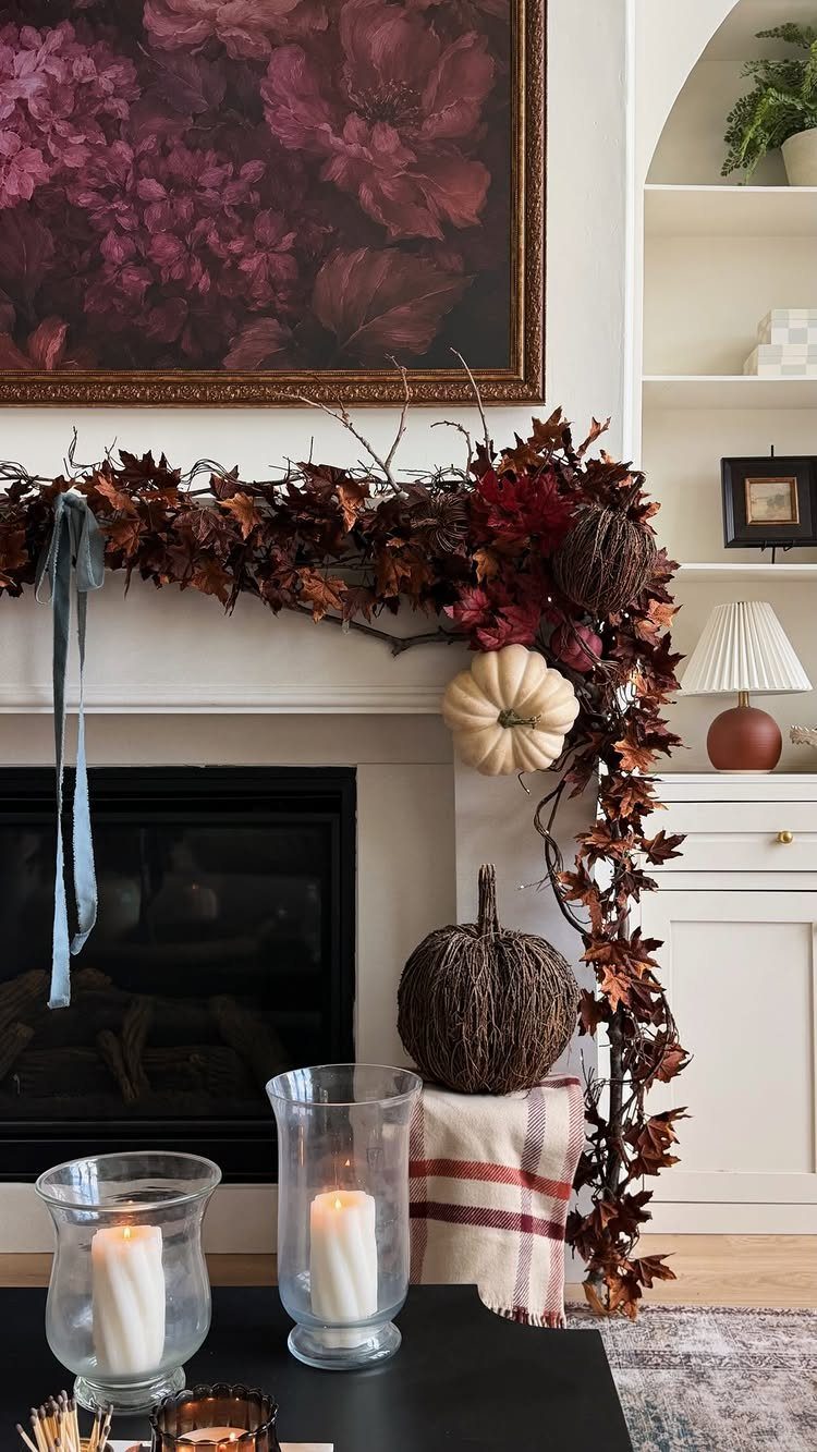 Fireplace mantel decorated with autumn leaves, pumpkins, and a dark floral painting above.