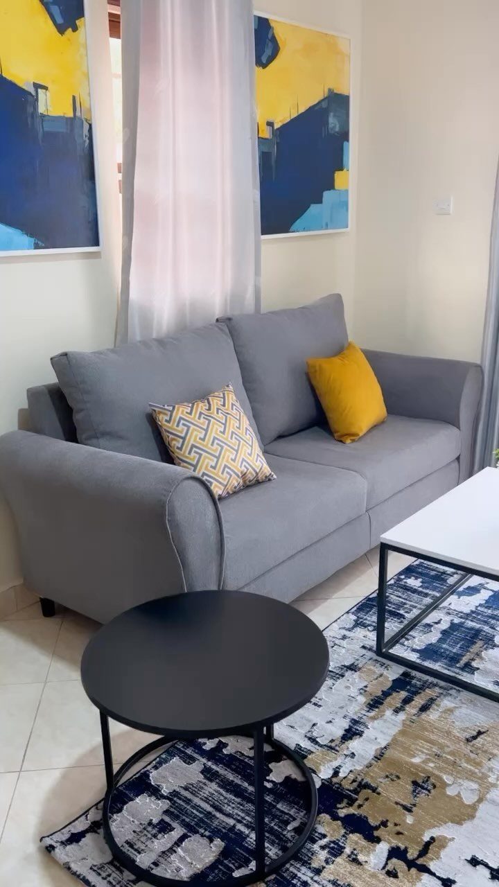 Grey sofa and small tables in a compact living room with abstract art.