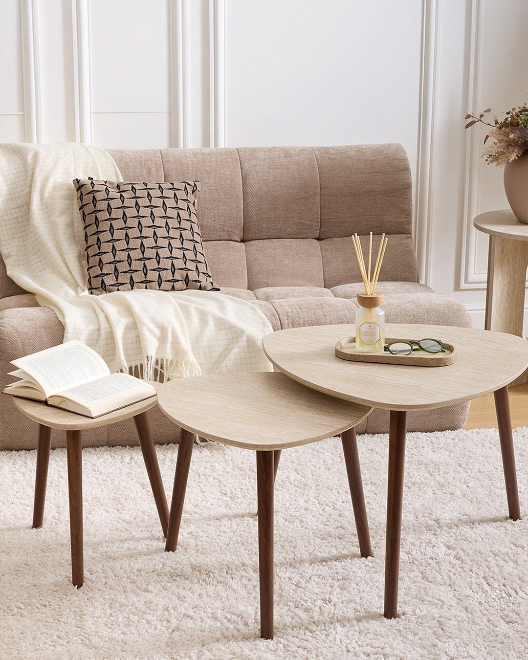 Three light-wood nesting tables of different sizes in a bright living room.