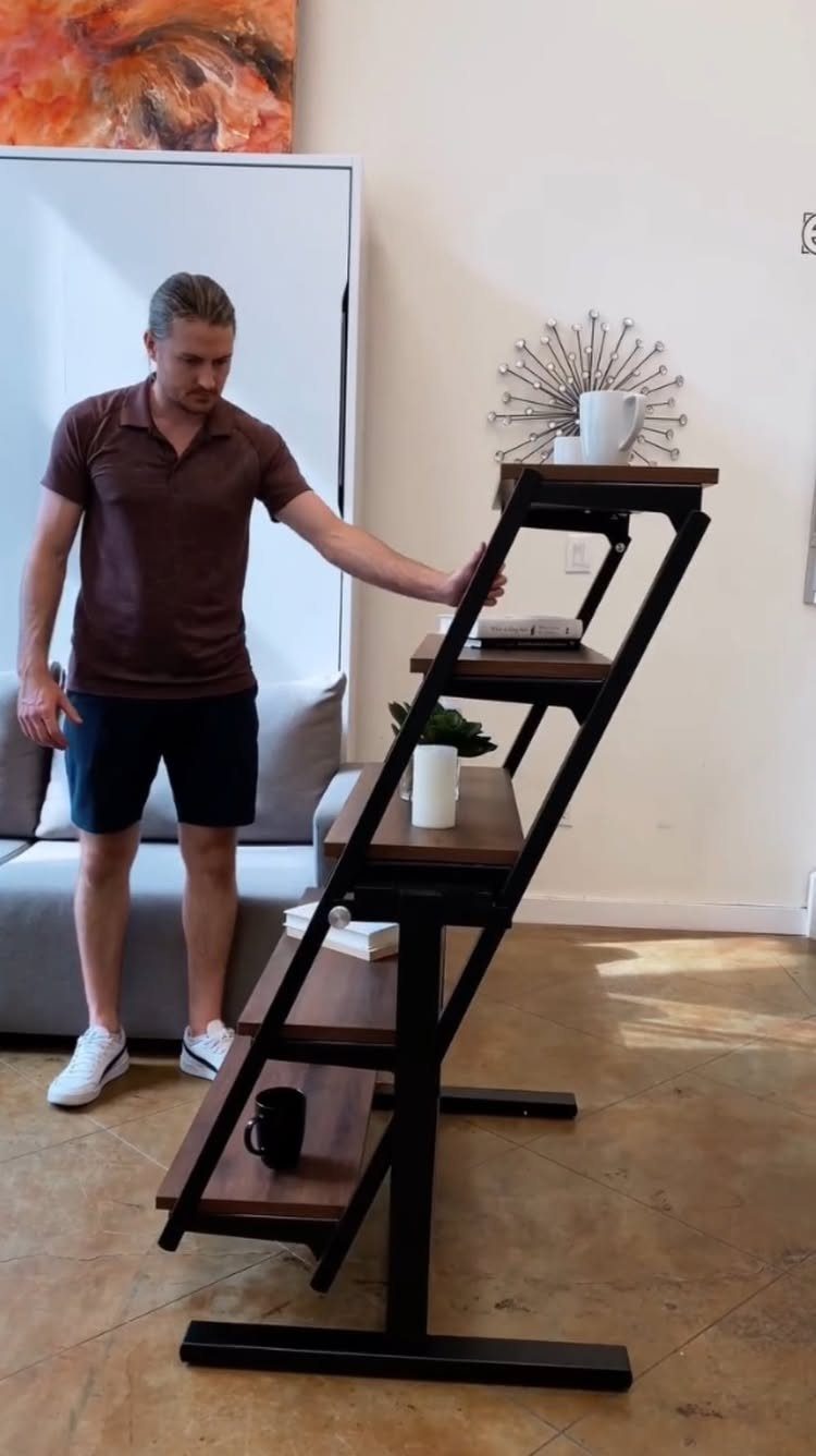 Man standing next to a multi-tiered slanted wooden shelf in a living room