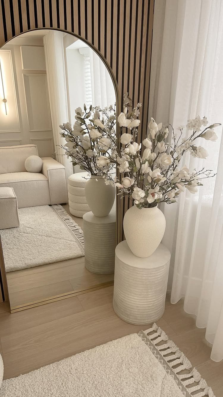 Arched mirror reflecting a bright living room with white flowers and neutral decor.