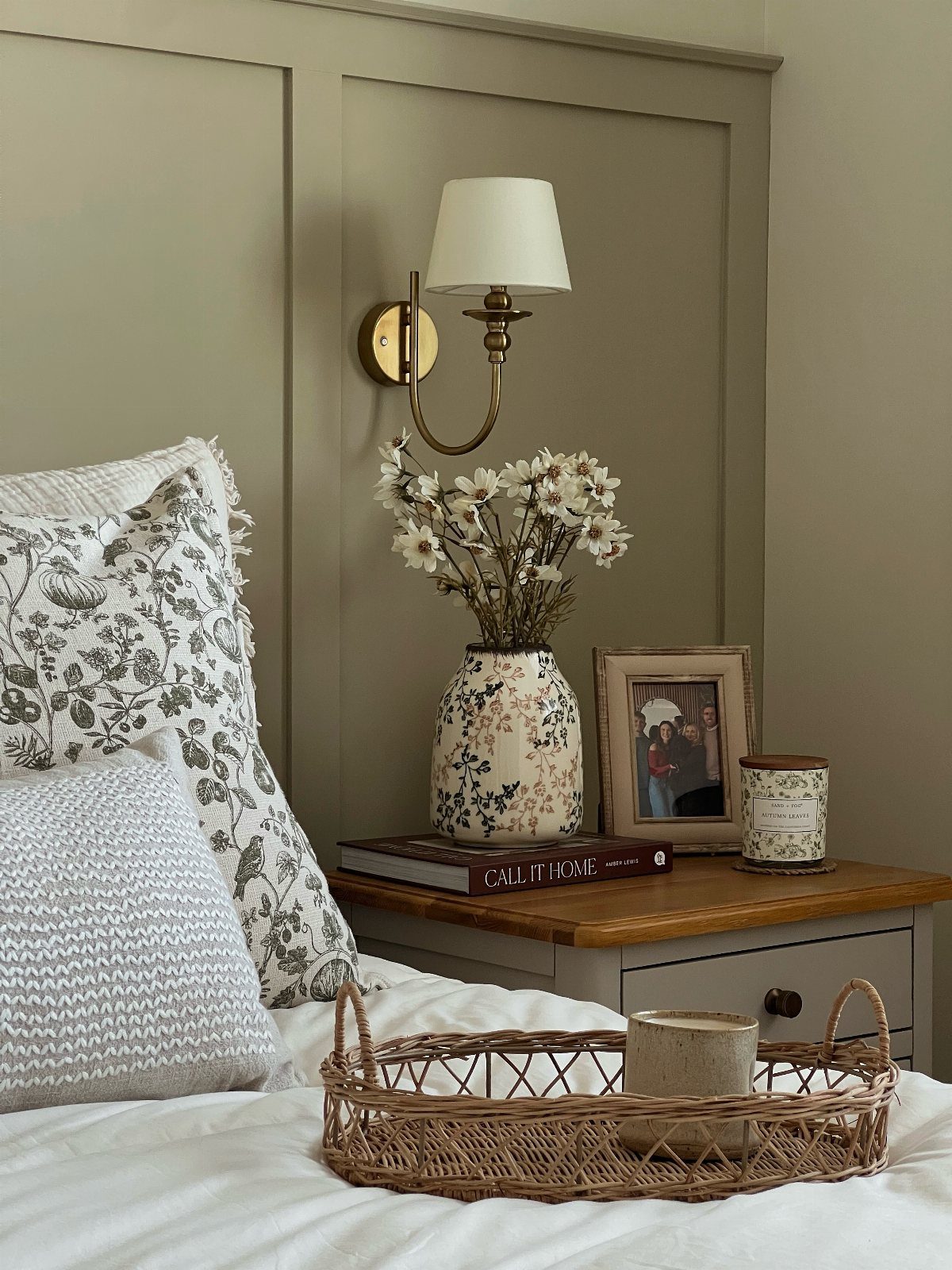 Bedside table with a framed photo, flower vase, and gold wall sconce lamp.