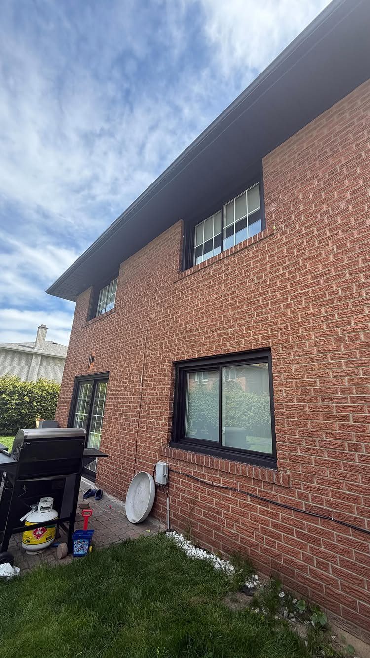 Red brick house exterior with black window trim and a black outdoor grill.