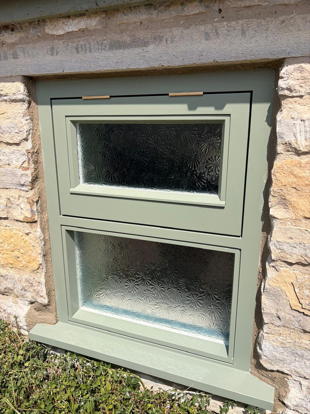 Sage green window frame with frosted glass set in a stone wall