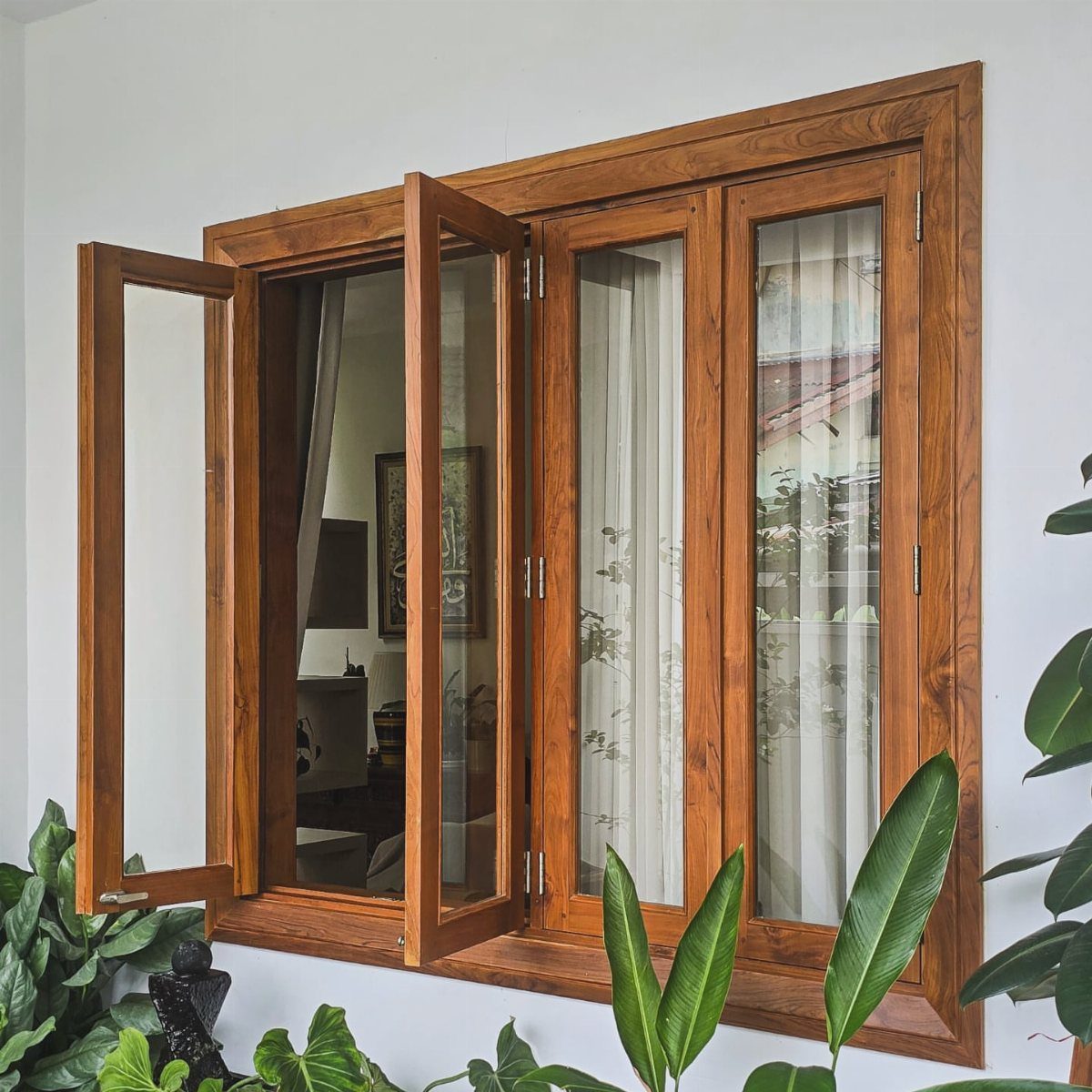 Wooden window with natural brown trim set in a white wall with green plants.