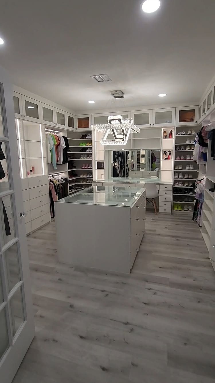 White walk-in closet with open shelving, clothing racks, and a central storage island.